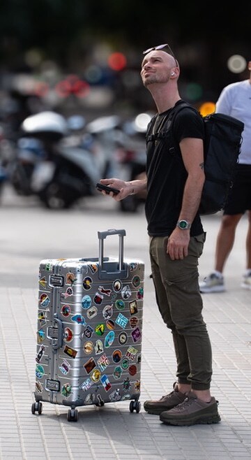 Traveler standing beside a sticker-covered suitcase