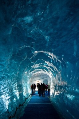 Visitors walking through a blue ice tunnel
